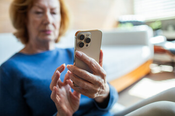 Senior woman smiling while using smartphone at home in bright living room