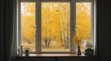 Autumn view through a window showing yellow trees and cozy indoor decorations
