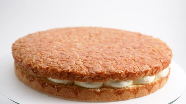 Round honey cake with almonds and white filling. The cake rotates on a white background.