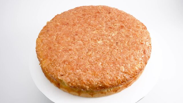 Round honey cake with almonds and white filling. The cake rotates on a white background.
