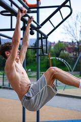 Young Man Doing Hanging Leg Raise Workout Outdoors. Athletic man performs hanging leg raises on an...