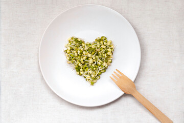 Young mung bean sprouts in the shape of a heart on a white plate on the table, top view. Healthy eating concept