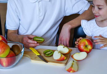Brother and Sister Preparing Fresh Fruit Together. Happy siblings in the kitchen cutting kiwi and apples, sharing a healthy moment together