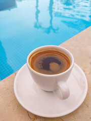 Turkish morning coffee in traditional white ceramic cup at swimming pool.
