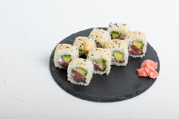 Close-up of sushi California rolls with fresh tuna, avocado, and sesame seeds on a black slate plate. Minimalist background with soft lighting.