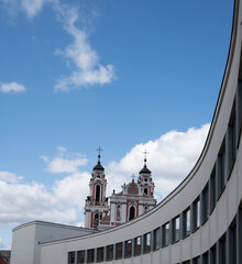 ornate red-white baroque twin-tower church rises behind a sweeping curved modern office block...
