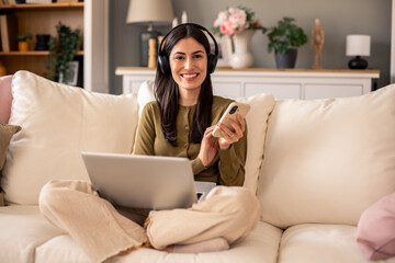 Smiling Woman Wearing Headphones While Using Laptop in a Warm and Inviting Living Room