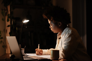 Young African businesswoman writing notes at her office desk at night