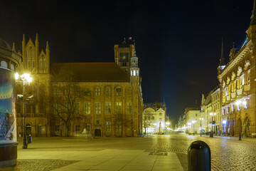 Night views of illuminated medieval city walls, gates and historic buildings in Toruń Old Town, Poland..