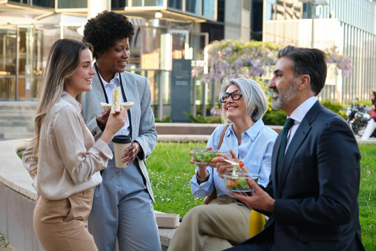 Multi ethnic colleagues eating healthy food and talking during lunch break in a green area of the business district - Powered by Adobe