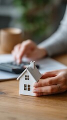 Hands holding a miniature house model on a wooden desk, possibly related to real estate or home financing