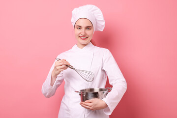 Confectioner in uniform with whisk and cooking pot on pink background