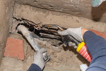 Plumber working with blowtorch and pipes, fixing and repairing leaky pipe in wall recess