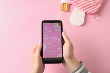 Menstruation. Woman holding smartphone with period calendar application on pink background, top view