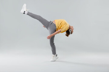 Girl with headphones in stylish clothes dancing on light grey background