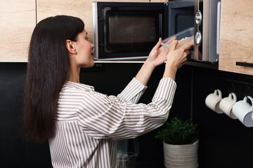 Woman putting container with lunch into microwave indoors