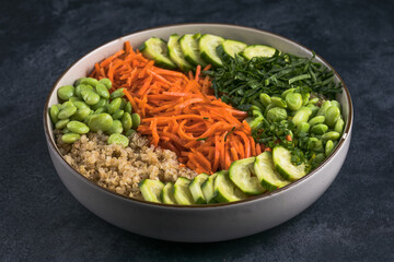 Vegan Poke bowl with quinoa,  edamame beans, cucumber and carrots in a gray bowl. Hawaiian ahi poke bowl, gray background.