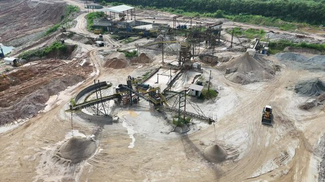 Vista a&eacute;rea de usina de minera&ccedil;&atilde;o com esteiras, britadores e escavadeiras. Processamento de areia e brita em ambiente industrial a c&eacute;u aberto, cercado por &aacute;reas de extra&ccedil;&atilde;o e vegeta&ccedil;&atilde;o