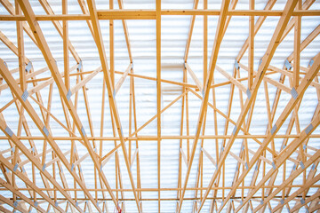 Detailed view of a wooden truss system with geometric beams and metal connectors supporting a corrugated translucent roof, allowing light to filter through.