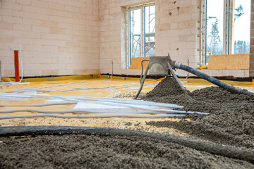 An under construction interior with light brick walls, concrete pouring via a hose, yellow floor...