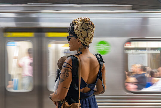 Tattooed mom with baby standing on S&atilde;o Paulo subway platform as train arrives, candid street scene