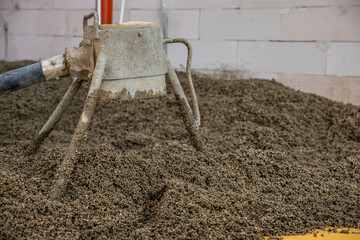 A weathered concrete mixer tool rests in a pile of aggregate material near a partially built brick...