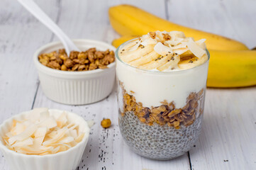 Chia pudding on coconut milk in a glass with banana on a light wooden background. Horizontal. Healthy breakfast, healthy lifestyle.