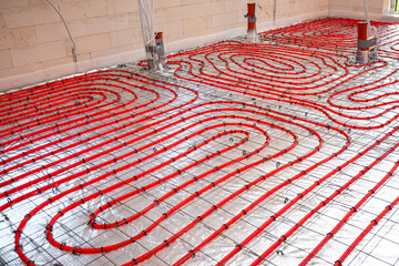 Interior of a construction site showing red underfloor heating pipes arranged in a spiral pattern on a metallic mesh over reflective insulation.
