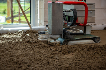A concrete leveling machine with a red handle operates on wet material indoors. Natural light...
