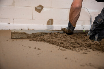 A worker uses a leveling tool to smooth Estrich concrete over underfloor heating pipes. Partially...