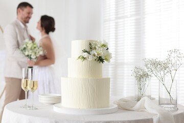 Happy married couple together indoors, focus on wedding cake and glasses of champagne on table