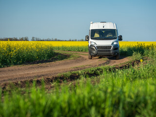 view to white commercial minibus on farm road between rapeseed fields in spring day