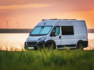 white camper van on grass meadow on the beach with sea view in sunset time