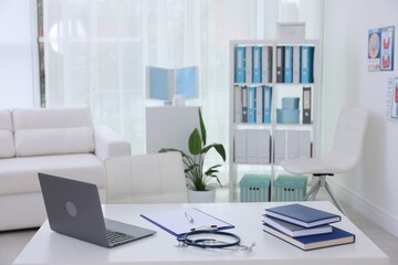 Laptop, stationery and stethoscope on desk in doctor's office