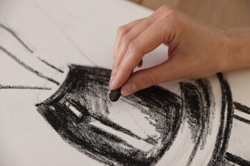 Obraz premium Woman drawing picture with black wax crayon on paper at table in artist's studio, closeup
