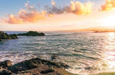 beautiful coast beach with sea gulf water during sunset or sunrise with golden sand, nice black rocks and stones, colorful vawes and clouds in thr sky