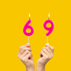 Hands holding birthday candles with number 69 - Yellow background