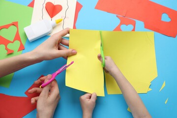 Mother and daughter making handmade project at light blue table, top view