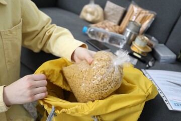 Survival kit. Woman putting raw pasta into backpack indoors, closeup
