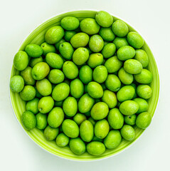 plate with fresh green olives on monochrome yellow background. Olive dish closeup, foor and drink concept