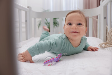 Fototapeta premium Cute little baby with rattle toy in crib at home