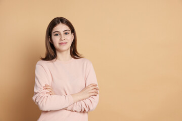 Fototapeta premium Portrait of beautiful teenage girl with crossed arms on beige background. Space for text