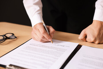 Man putting signature on document at wooden table, closeup