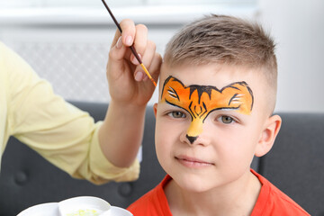 Animator drawing tiger on boy's face indoors, closeup