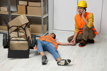 Accident at work. Man calling ambulance for his unconscious colleague in warehouse
