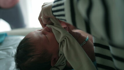 Fototapeta premium Mother tenderly caring for her newborn baby, dressing the baby in clothing, capturing an intimate moment of maternal care and love in a softly lit indoor environment