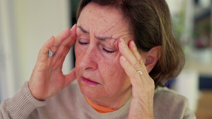 Woman experiencing severe headache, pressing fingers to temples with a tense expression. Closed...