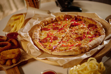 Serving pepperoni pizza on wooden tray alongside breaded onion rings, fries, and soft drink. Warm and inviting ambiance enhancing appetite