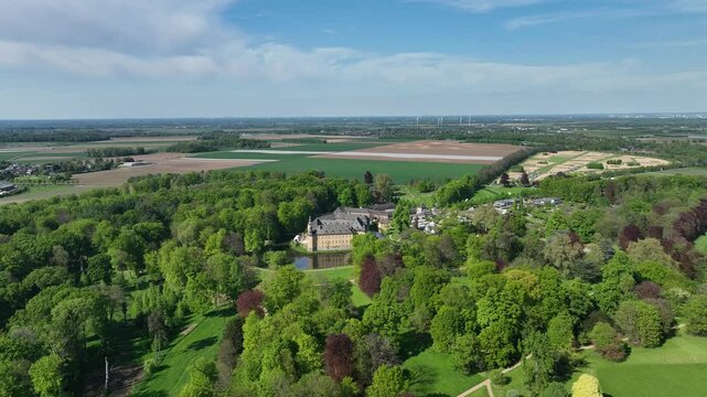 Panoramic drone flight over Schloss Dyck and its blooming parkland near Grevenbroich, Germany: sweeping aerial views of gardens, orchards, fields, and historic architecture in spring.