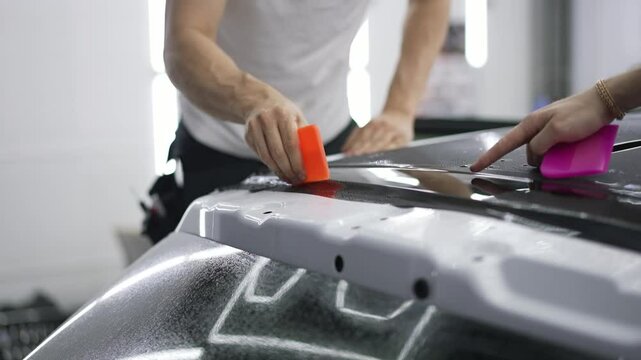 Car service technician applying vinyl foil or film on a vehicle spoiler to protect the paint from scratches and stone chips